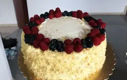 Pyszny tort śmietankowo-malinowy z mascarpone, ozdobiony świeżymi malinami i borówkami, posypany złotymi i srebrnymi kuleczkami.