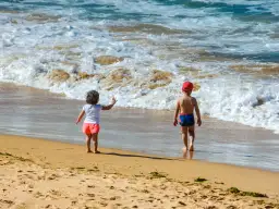 Dzieci w strojach kąpielowych dwuczęściowych dla dzieci bawią się na plaży, machając do fal.