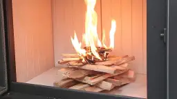 Ogień płonie na ułożonych szczapach drewna. Dowiedz się, jak rozpalić w kominku bez podpałki, używając tylko drewna.