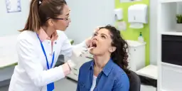 Lekarka bada gardło pacjentki drewnianym patyczkiem.
