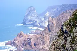 Skaliste wybrzeże Cabo da Roca, z falami rozbijającymi się o klify, w oddali widać mgliste góry.