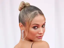 Elegancka kobieta z blond włosami spiętymi w wysoki kok. Jej **ulizane włosy** idealnie podkreślają rysy twarzy i błyszczące kolczyki.