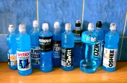 Rząd niebieskich butelek z napojami izotonicznymi i sportowymi na drewnianym blacie.