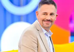 Krzysztof Ibisz, znany z programów telewizyjnych, uśmiecha się w beżowej marynarce. Jego wiek dodaje mu charyzmy.
