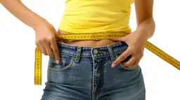 Kobieta mierzy talię żółtą miarką krawiecką na tle białym.
