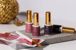 Trzy buteleczki lakierów hybrydowych Boska Nails z złotymi nakrętkami, pędzelek i ozdobna kula.