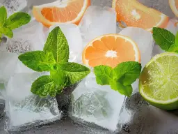 Jak zrobić krystaliczny lód w domu? Kostki lodu, plasterki pomarańczy, limonki i listki mięty tworzą orzeźwiającą kompozycję.