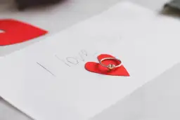 Pierścionek z serduszkiem na czerwonym sercu, obok napis "I love you". Idealne życzenia walentynkowe po angielsku.