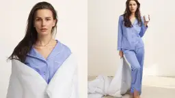 Kobieta w niebieskiej piżamie bawełnianej, owinięta kołdrą, trzyma kubek.