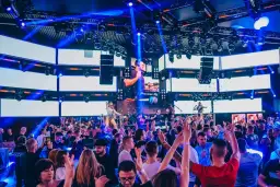 Koncert DJ-a w klubie z tłumem bawiących się ludzi i efektami świetlnymi.