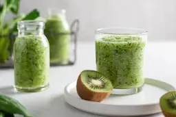 Zielony koktajl w szklance i butelkach, z połówkami kiwi na talerzyku.