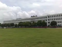 Ogromny budynek City Montessori School, być może największa szkoła na świecie, z zielonym boiskiem przed nim.