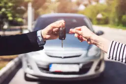 Przekazanie kluczyków do auta. Nowy właściciel cieszy się z zakupu, a sprzedający upewnia się, że wszystko jest w porządku, jak przy ubezpieczeniu OWU AC PZU.