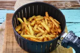 Koszyk frytkownicy wypełniony złocistymi, pofalowanymi frytkami.