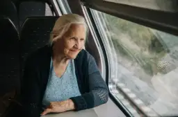 Starsza pani wpatruje się w krajobraz za oknem pociągu Pendolino, zastanawiając się, czy na pendolino są zniżki dla emerytów.
