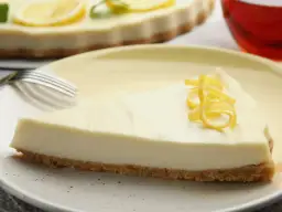Kawałek puszystego sernika cytrynowego z kruchym spodem, ozdobiony skórką cytrynową. Idealny na deser.