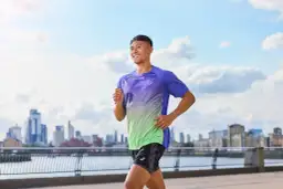 Uśmiechnięty mężczyzna w sportowym stroju biegnie nad rzeką, z panoramą miasta w tle. Czy warto biegać? Ten widok mówi wszystko!