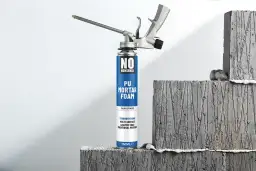 Pistolet do pianki montażowej "No Nonsense" gotowy do pracy, obok betonowych bloków.