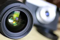 Obiektyw aparatu z widocznymi odbiciami, gotowy do uchwycenia wyjątkowych chwil. To symbol akredytacji fotograficznej.