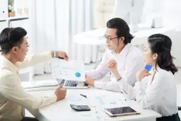 Zespół analizuje dane, omawiając potencjalną cesję polisy. Na stole leżą dokumenty, laptop i kalkulator.