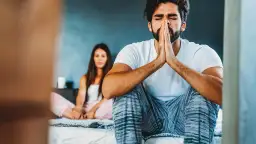 Zmartwiony mężczyzna z rękami złożonymi do modlitwy, siedzi na łóżku. Obok niego kobieta. Co robić gdy facet patrzy na inne?