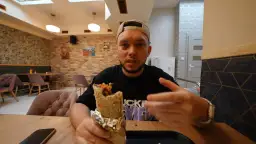 Mężczyzna z kebabem w ręku, zastanawia się, czy to bajka, czy alibaba. W tle restauracja.