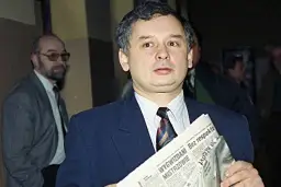 Jarosław Kaczyński, jeden z tych, kto założył PiS, trzyma gazetę. Obok stoi mężczyzna w okularach.