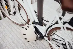 Biały rower zabezpieczony U-lockiem. Kask rowerowy wisi na ramie. Zastanawiasz się, jak otworzyć zapięcie do roweru bez klucza?