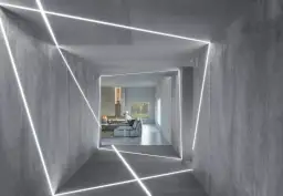 Nowoczesny korytarz z betonowymi ścianami i geometrycznym podświetleniem ściany od dołu. W tle salon z kominkiem i widokiem na zieleń.