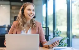 Uśmiechnięta konsultantka z branży SEO, pracująca przy laptopie i tablecie, z zestawem słuchawkowym na głowie.