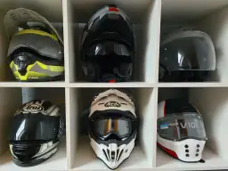 Sześć kasków motocyklowych w różnych kolorach i stylach, ułożonych w sześciu przegrodach.