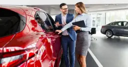 Para jak negocjować cenę samochodu w salonie, ogląda lśniący, czerwony pojazd. Sprzedawca z uśmiechem wskazuje na detale.