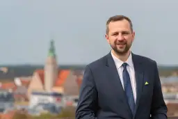 Mężczyzna w garniturze uśmiecha się na tle panoramy miasta z wieżą.