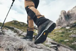 Turysta stawia kroki na kamienistym szlaku, jego buty z podeszwami Vibram zapewniają pewność na nierównym terenie.
