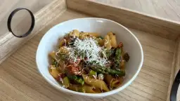 Penne z zielonymi szparagami i suszonymi pomidorami w kremowym sosie, posypane parmezanem. Pyszne danie na drewnianej tacy.