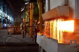 Gorący metal spływa podczas wyżarzania stali. Pracownicy w hełmach nadzorują proces w hucie.
