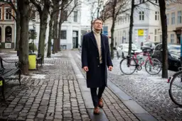 Elegancki mężczyzna w granatowym płaszczu i golfie spaceruje po zimowej ulicy. Stylowe granatowy płaszcz stylizacje na chłodne dni.