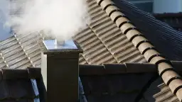 Dym wydobywający się z komina na dachu pokrytym dachówką.