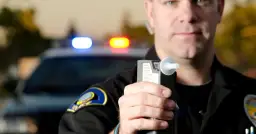 Policjant trzyma alkomat. Nie ma sposobu, jak dmuchać w alkomat żeby nie wykazało.