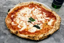 Pizza Margherita z roztopionym serem, sosem pomidorowym i bazylią na kamiennym blacie.