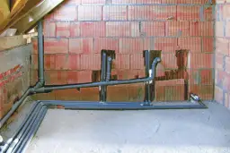 Instalacja hydrauliczna z rurami, zapewniająca minimalny spadek dla rury 160. Ściana z pustaków ceramicznych, podłoga betonowa, widoczne drewniane elementy konstrukcji dachu.