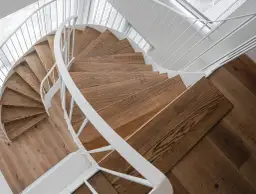 Drewniane schody kręcone z białymi poręczami, idealne, gdy zastanawiasz się, jak zrobić schody kręcone.