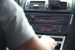 Ręka kierowcy manipuluje przy radiu BMW, pokazując jak ustawić radio w samochodzie. Widoczna temperatura 22°C.