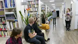 Grupa osób słucha opowieści o tym, że kto czyta książki żyje podwójnie, autor opowieści stoi w tle.