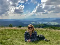 Uśmiechnięta kobieta leży na trawie na szczycie Mogielnicy, podziwiając malowniczy krajobraz gór.