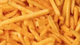 Zbliżenie na złociste, chrupiące frytki ułożone jedna na drugiej.