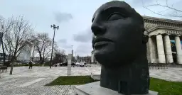 Duża, ciemna rzeźba głowy Igora Mitoraja na tle Teatru Dramatycznego w Warszawie.