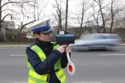 Policjantka w kamizelce odblaskowej mierzy prędkość przejeżdżającego samochodu radarem.