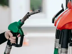 Dłoń trzyma zielony pistolet dystrybutora paliwa. Czy to benzyna 95 czy 98? Różnica jest ważna dla silnika.