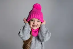 Uśmiechnięta dziewczynka w różowej czapce z pomponem i kominie. Idealne szaliki dla dzieci na zimowe zabawy.